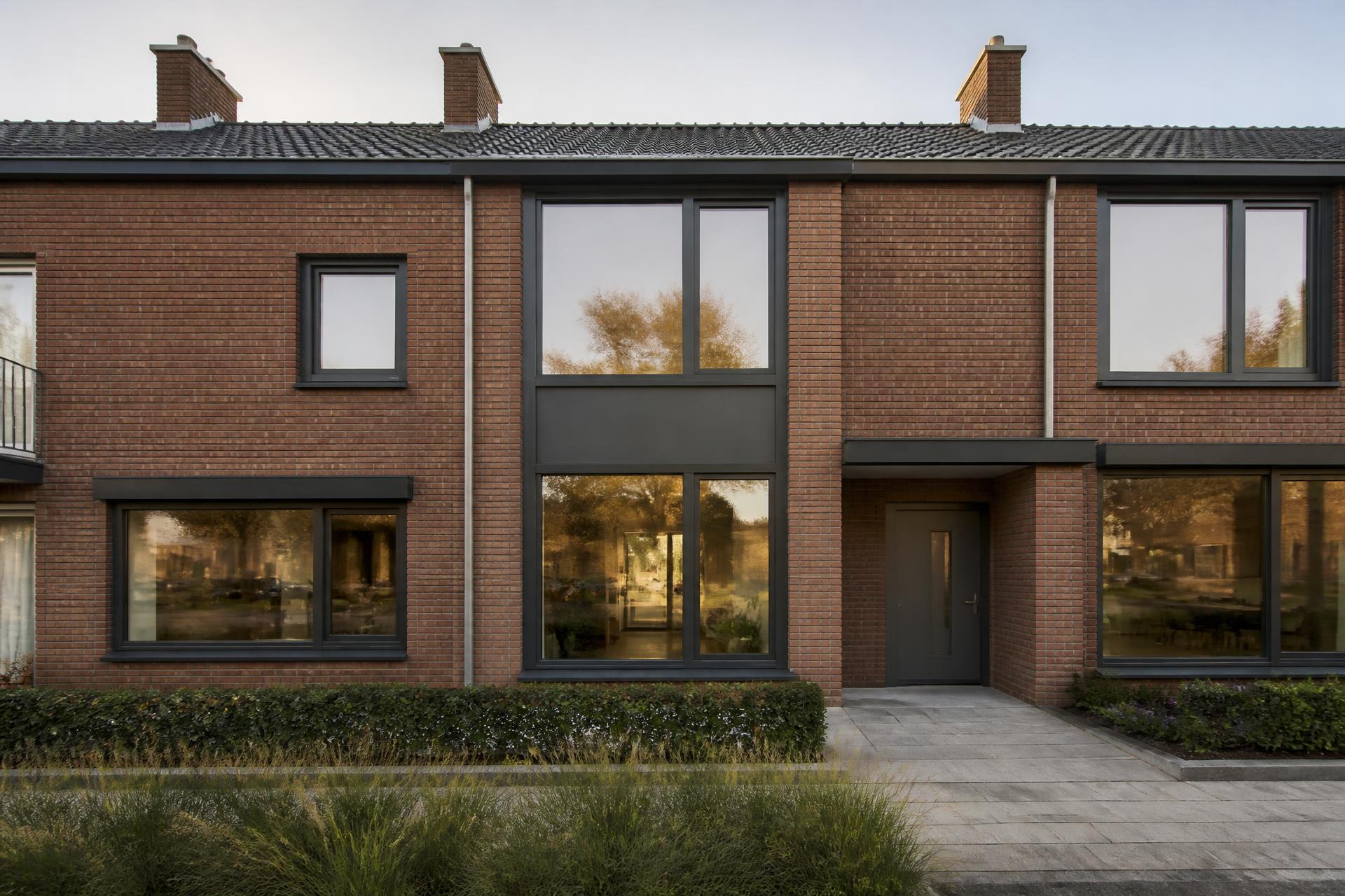Rijtjeswoning met antracietkleurige kunststof kozijnen en een grote pui in avondlicht